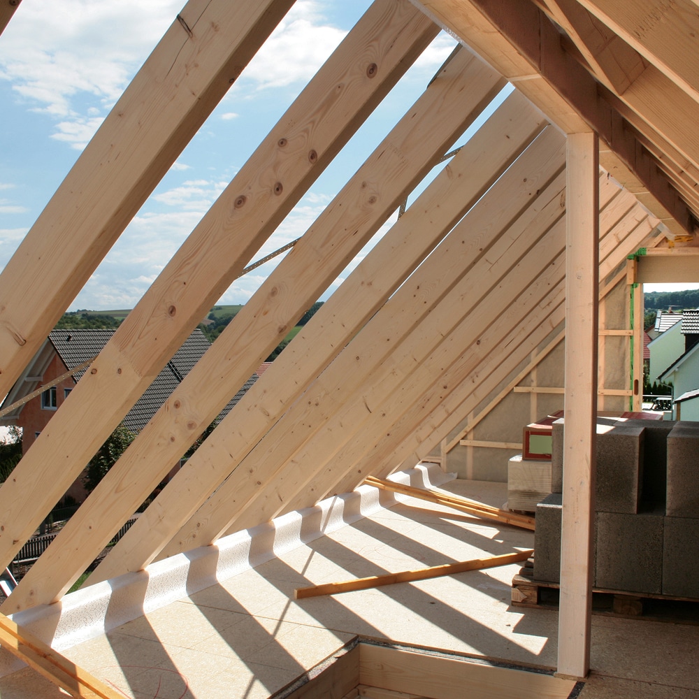 Charpente de toit en bois avec chevrons apparents et matériaux de construction dans des combles en chantier.