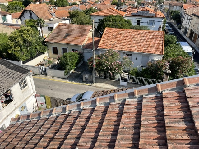 Vue plongeante sur toits en tuiles terre cuite et maisons de quartier résidentiel.